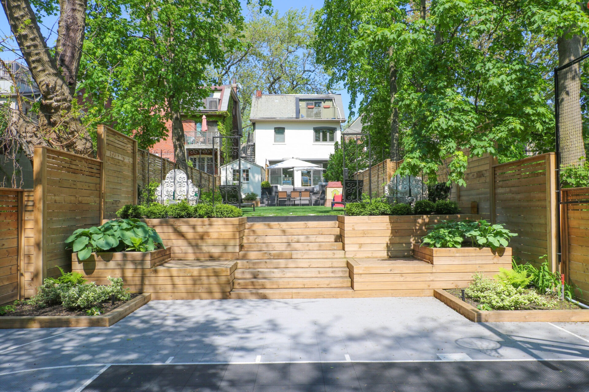 A backyard with a wooden deck, planters, and stairs leading to a house surrounded by trees. Charming garden area for relaxation.
