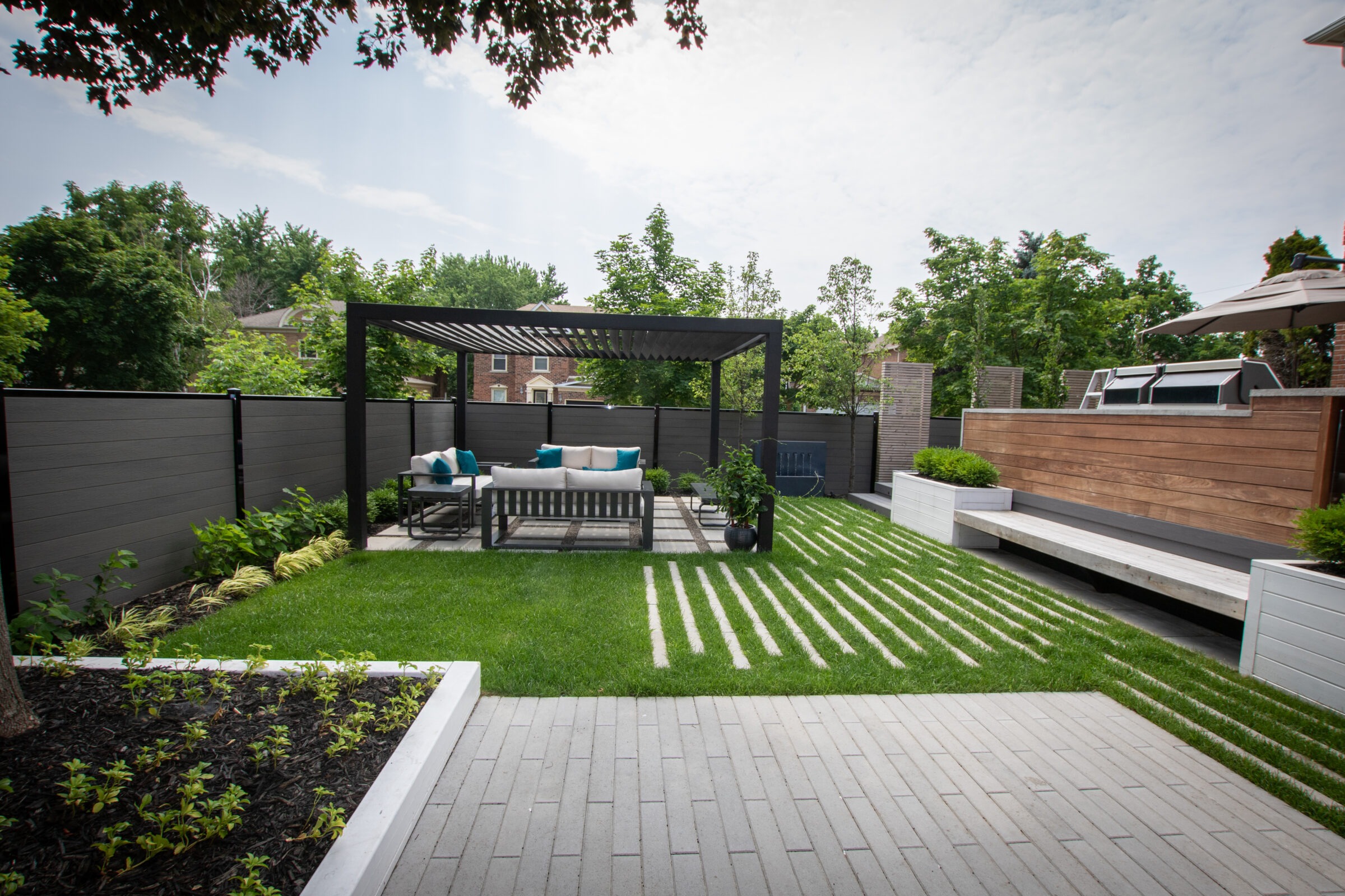 Modern backyard with pergola, outdoor seating, and neatly landscaped grass. Privacy fence surrounds the area, featuring contemporary design with clean lines and lush greenery.