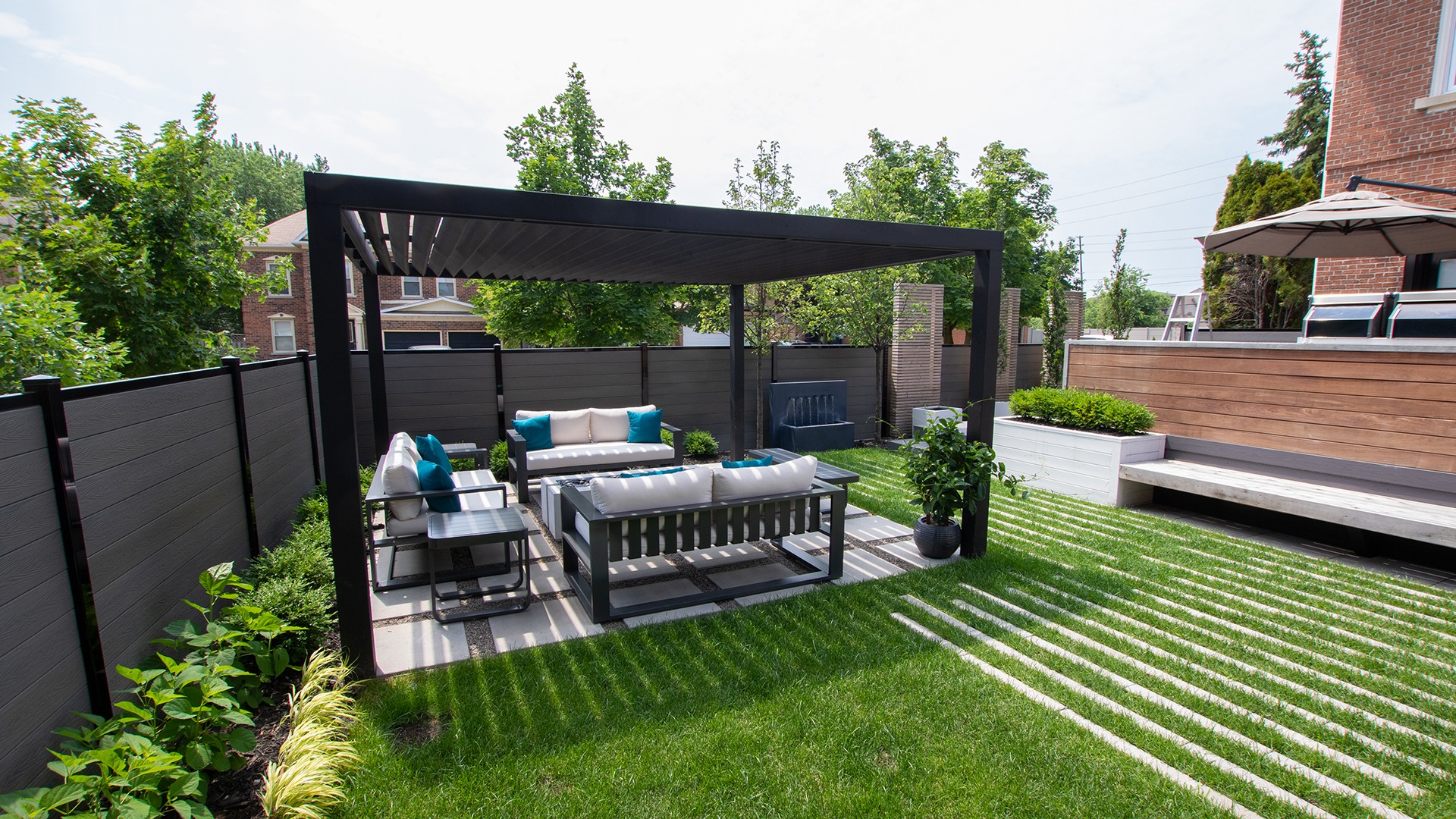 A modern backyard features a pergola with comfortable seating, surrounded by greenery and wooden fencing, creating a relaxing outdoor space.