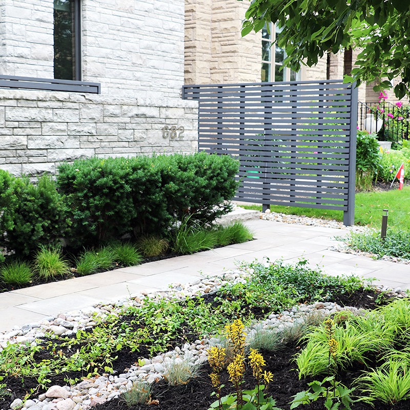 Modern garden with lush greenery, stone path, and contemporary gray fence. Brick house exterior displays address number 682 amidst well-maintained landscaping.
