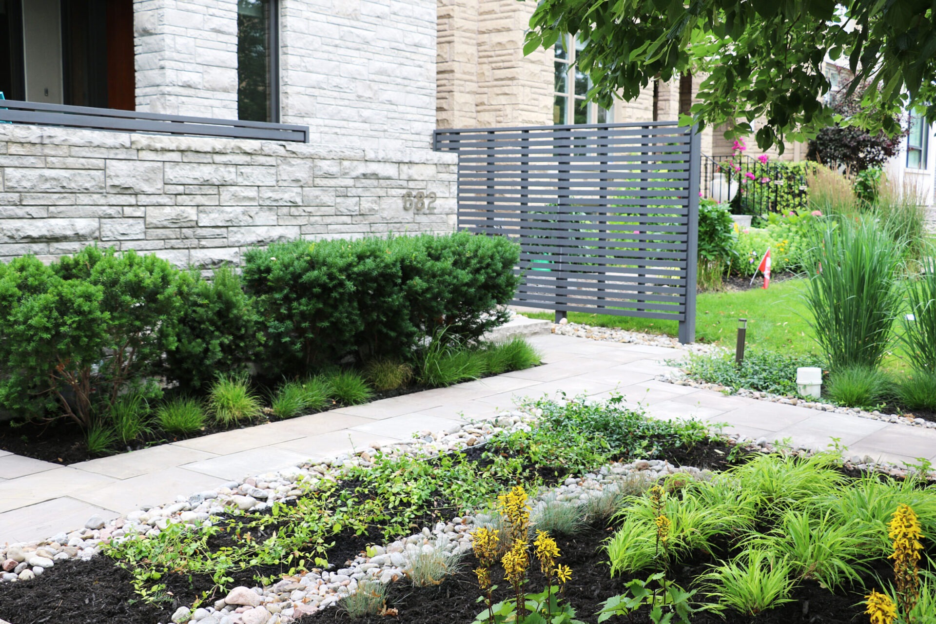 Modern building with stone facade features a lush, landscaped garden. Decorative plants and stones create a serene, well-maintained outdoor space.