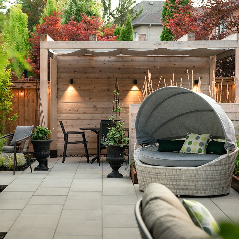 Modern patio with canopy chair, wooden pergola, and seating area. Surrounded by plants and shrubs, creating a cozy outdoor relaxation space.