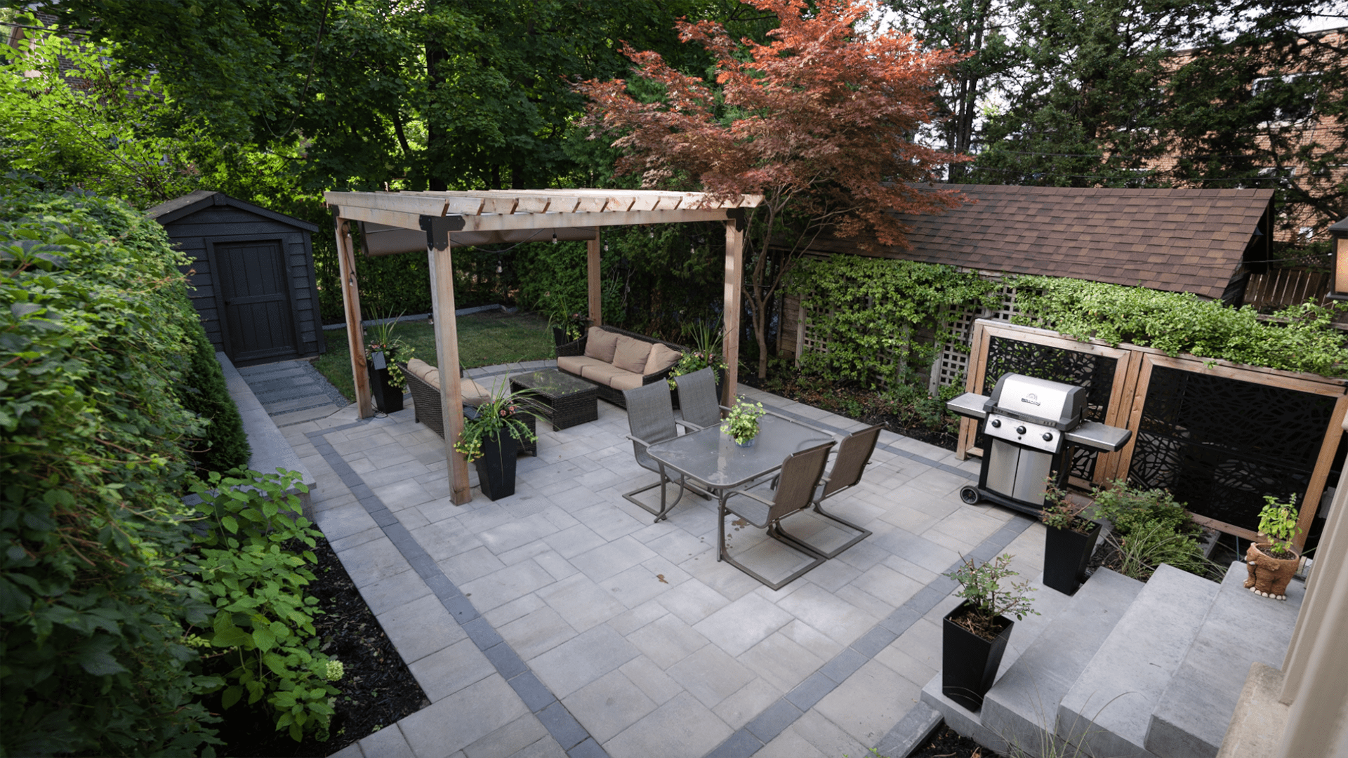 A backyard patio with a pergola, outdoor furniture, grill, and lush greenery. Cozy and inviting space for relaxation and gatherings.