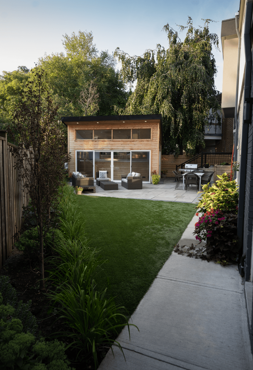 Modern backyard with green lawn, wooden shed, and patio seating. Surrounded by lush trees and plants, creating a peaceful outdoor retreat.