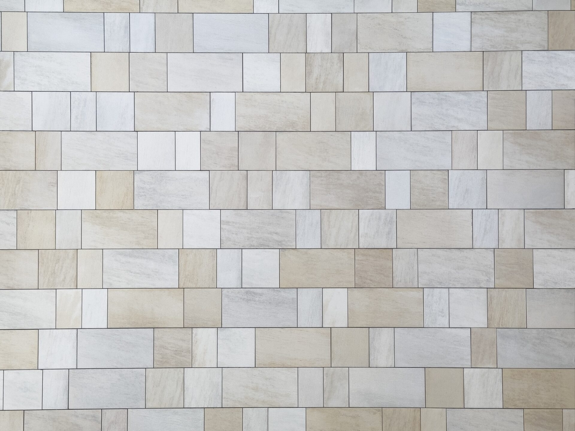 A uniform pattern of rectangular beige tiles, creating a neutral geometric wall design with subtle variations in shading and texture.