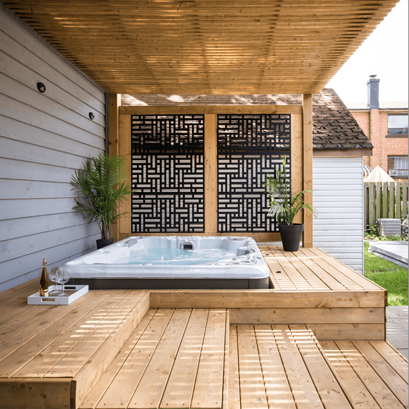 A backyard patio with a wooden deck features a hot tub, modern lattice design, potted plants, and a small tray with wine.
