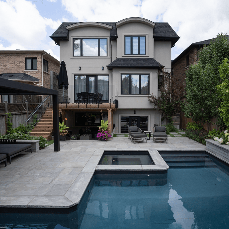 Contemporary home with a spacious backyard featuring a swimming pool, patio furniture, and elevated deck surrounded by neighboring houses and lush greenery.